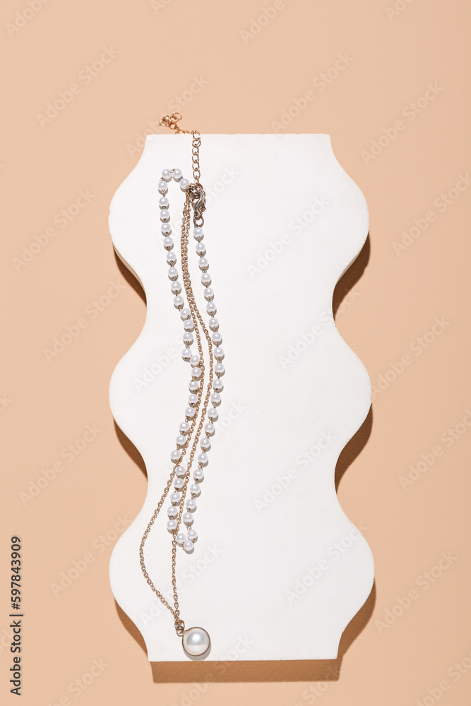 Showcase pedestal with golden necklaces on beige background