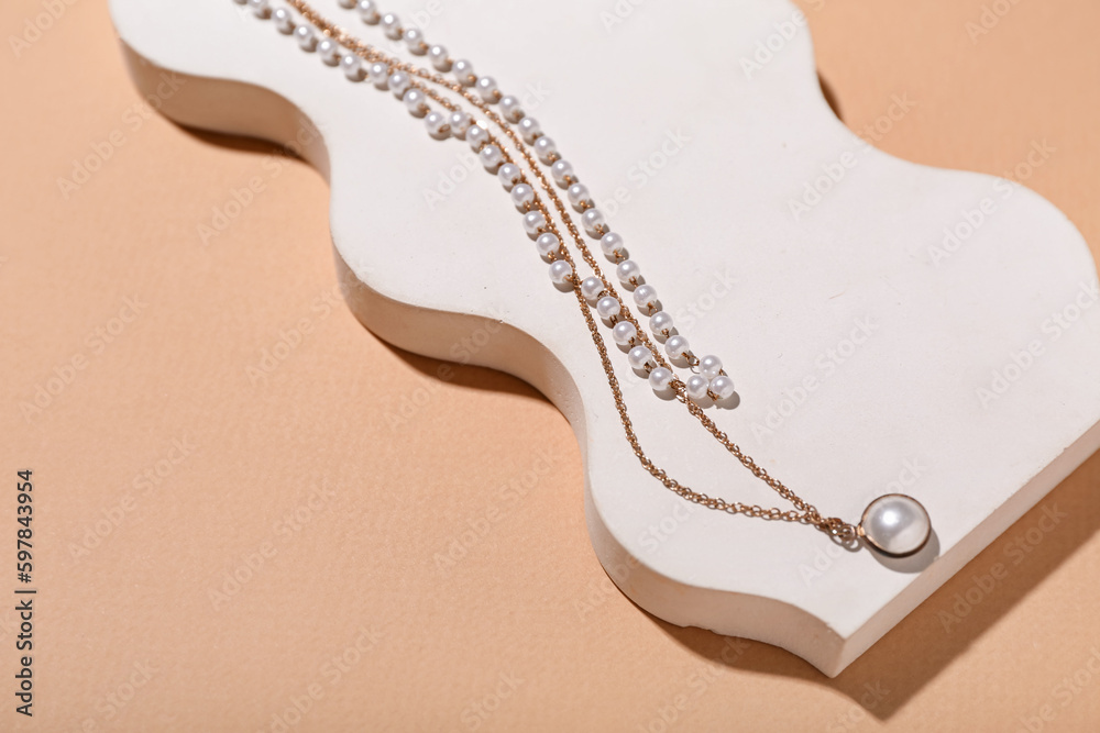 Showcase pedestal with golden necklaces on beige background, closeup