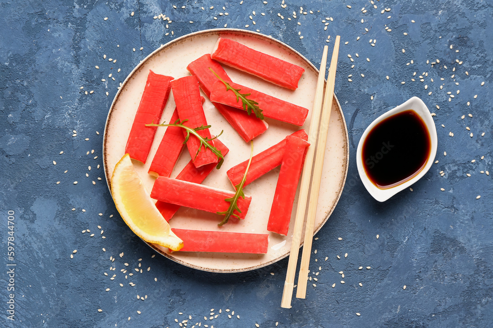 Plate with tasty crab sticks and sauce on blue background