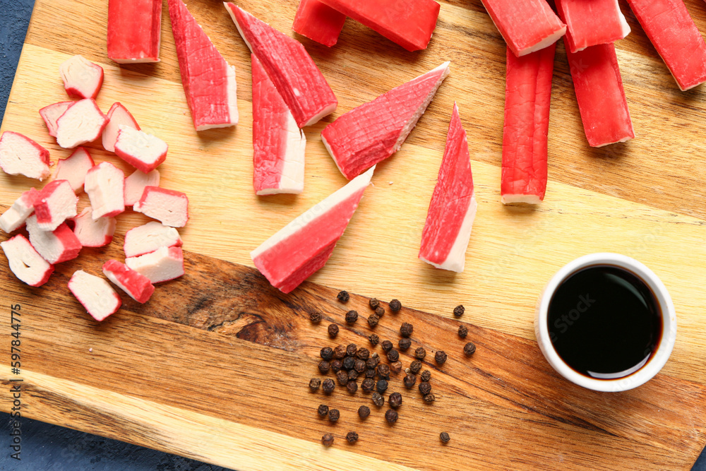 Wooden board with tasty crab sticks and sauce on table, closeup