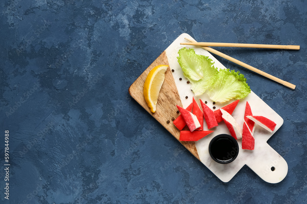 Board with tasty crab sticks and sauce on blue background