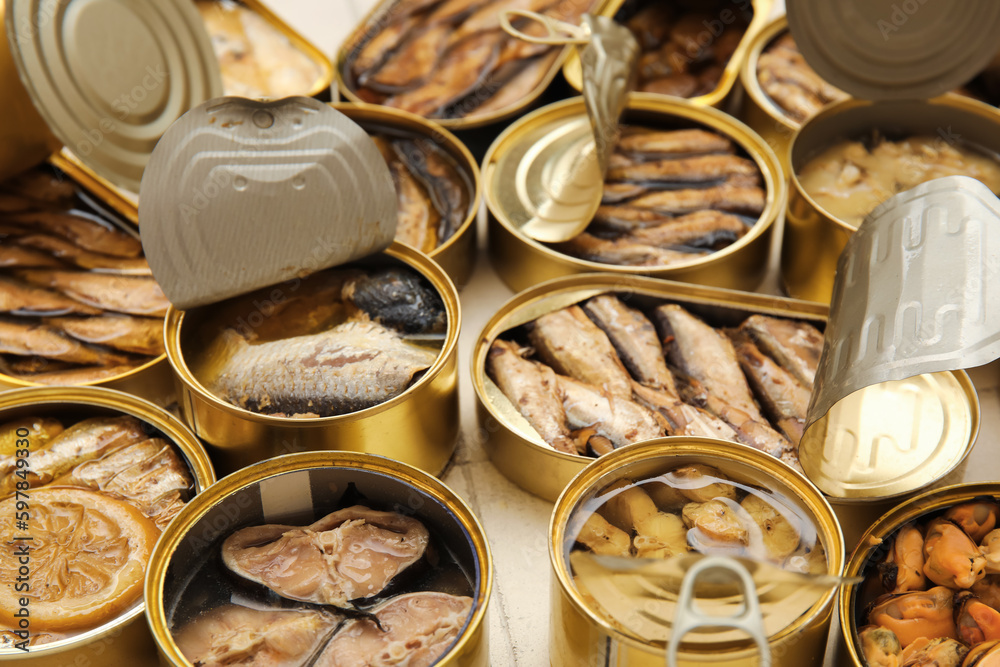 Many opened cans with different fish on tiled table, closeup