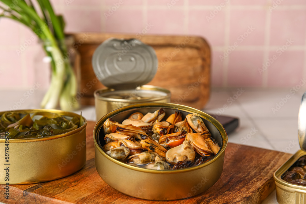 Board with opened tin cans of mussels on white tiled table