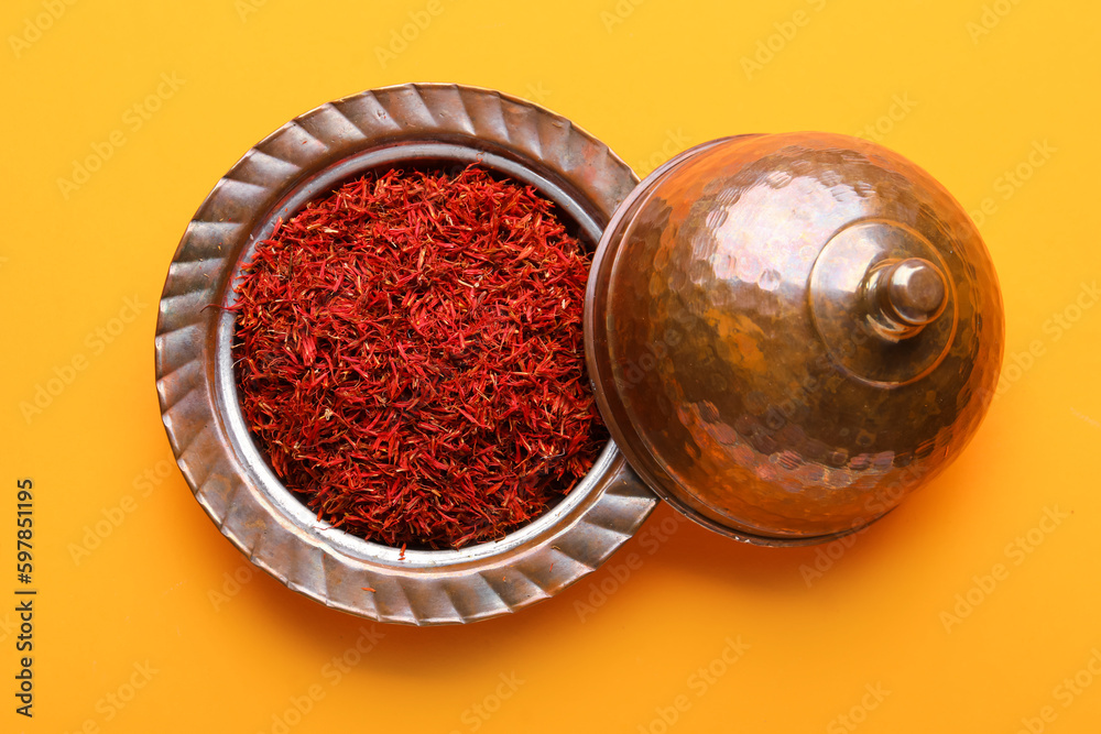 Bowl with pile of saffron on orange background