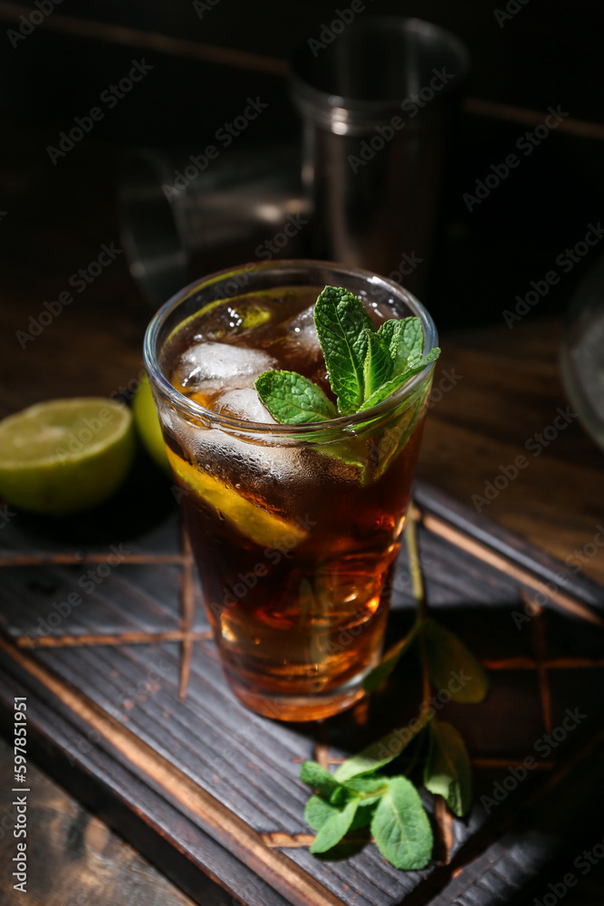 Glass of tasty Cuba Libre cocktail on dark wooden background