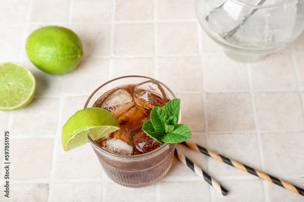 Glass of tasty Cuba Libre cocktail on light tile background