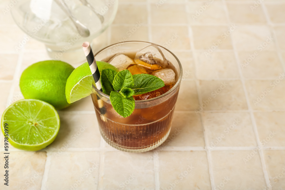 Glass of tasty Cuba Libre cocktail on light tile background