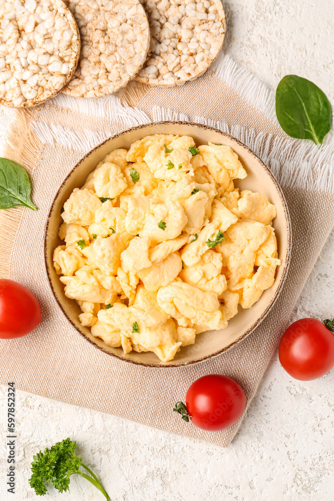 Composition with bowl of scrambled eggs and rice crackers on light textured background