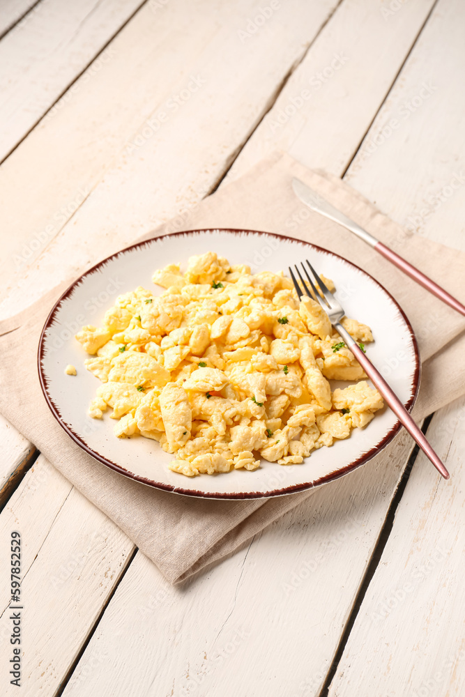 Plate of tasty scrambled eggs with cutlery on white wooden background