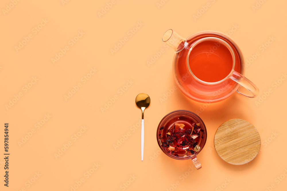 Transparent teapot and cup of fruit tea on orange background