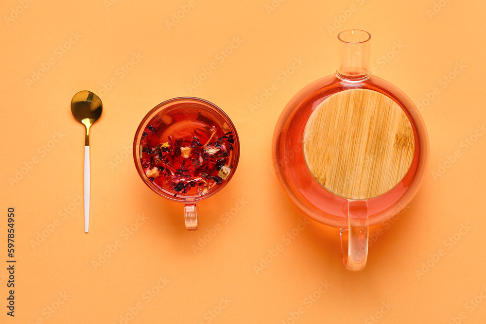 Transparent teapot and cup of fruit tea on orange background