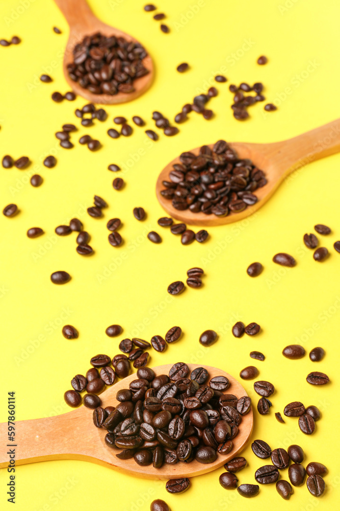 Wooden spoons with coffee beans on yellow background