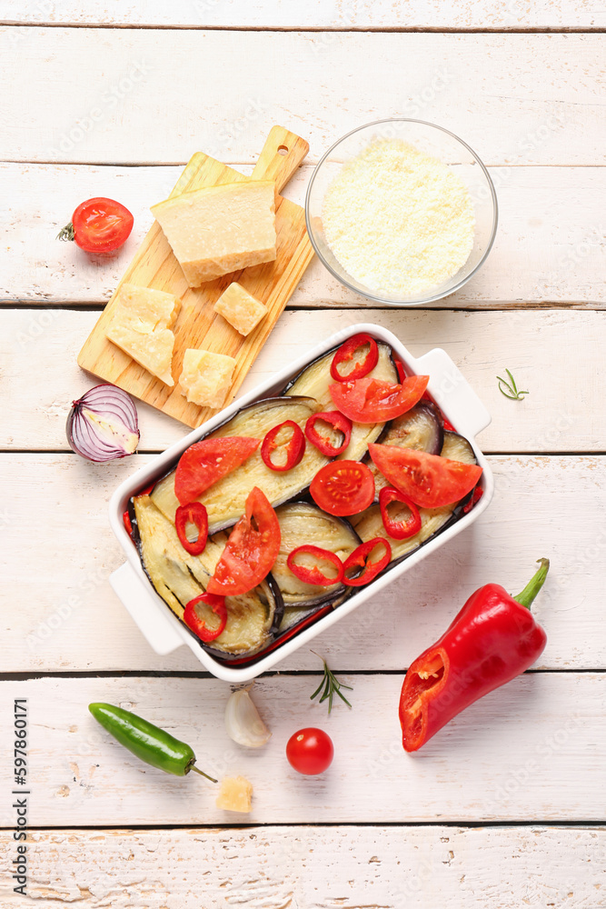 Baking dish with tasty Eggplant Parmesan and ingredients on light wooden background