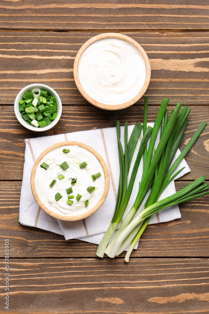 Bowls of tasty sour cream with green onion on wooden background