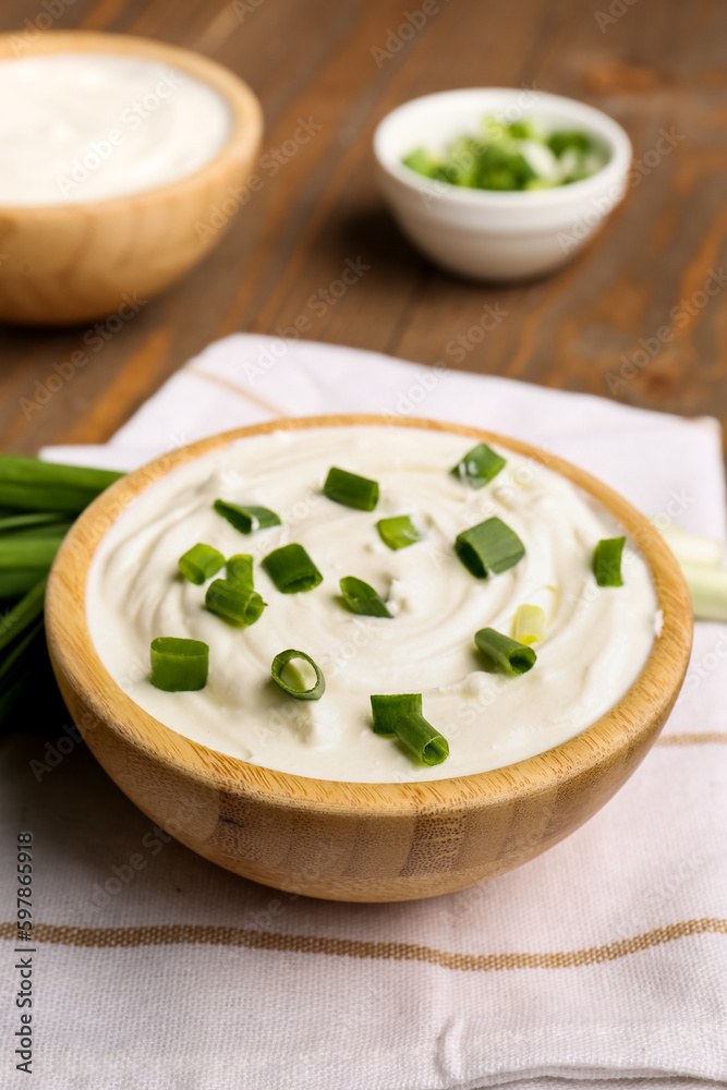 Bowl of tasty sour cream with green onion on table