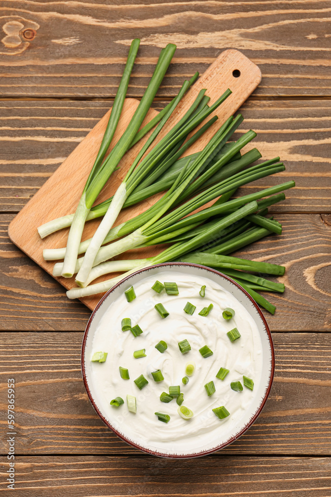 Bowl of tasty sour cream with green onion on wooden background