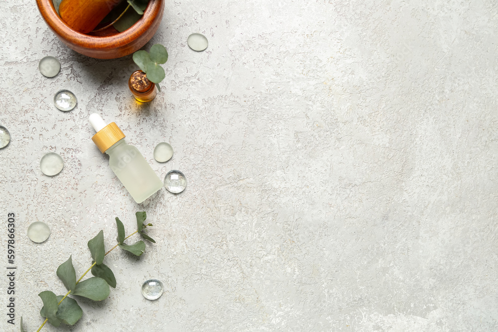 Cosmetic oil bottles with wooden mortar and pestle and eucalyptus branch on grey textured background