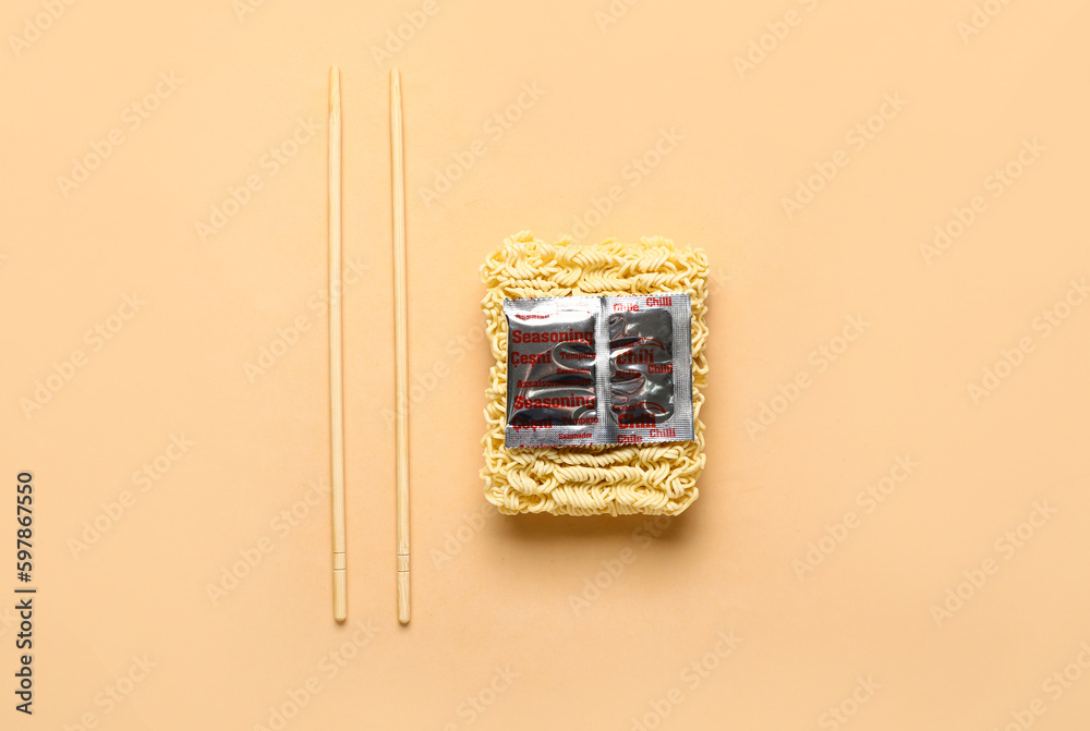 Raw instant noodles with chopsticks and seasoning on beige background