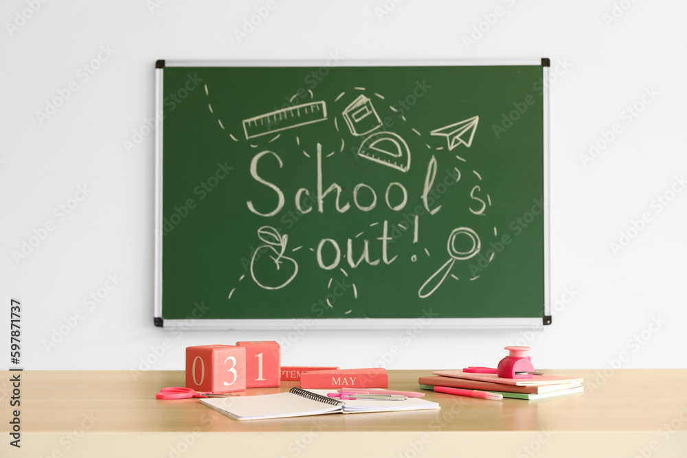 Blackboard with text SCHOOLS OUT, drawings and desk in classroom