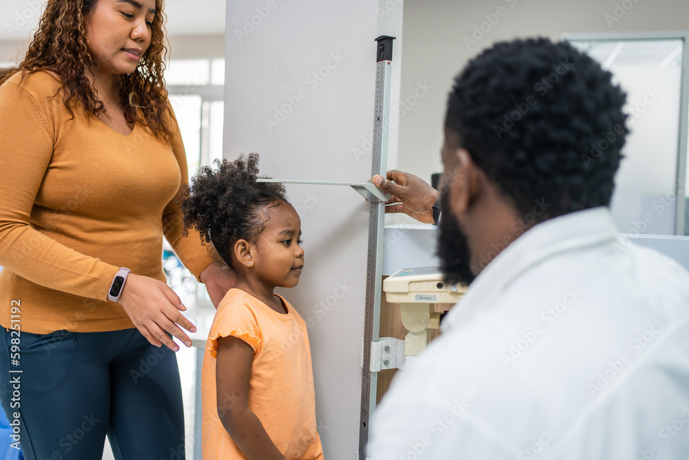 Mature doctor measuring black African little girls height in hospital. 