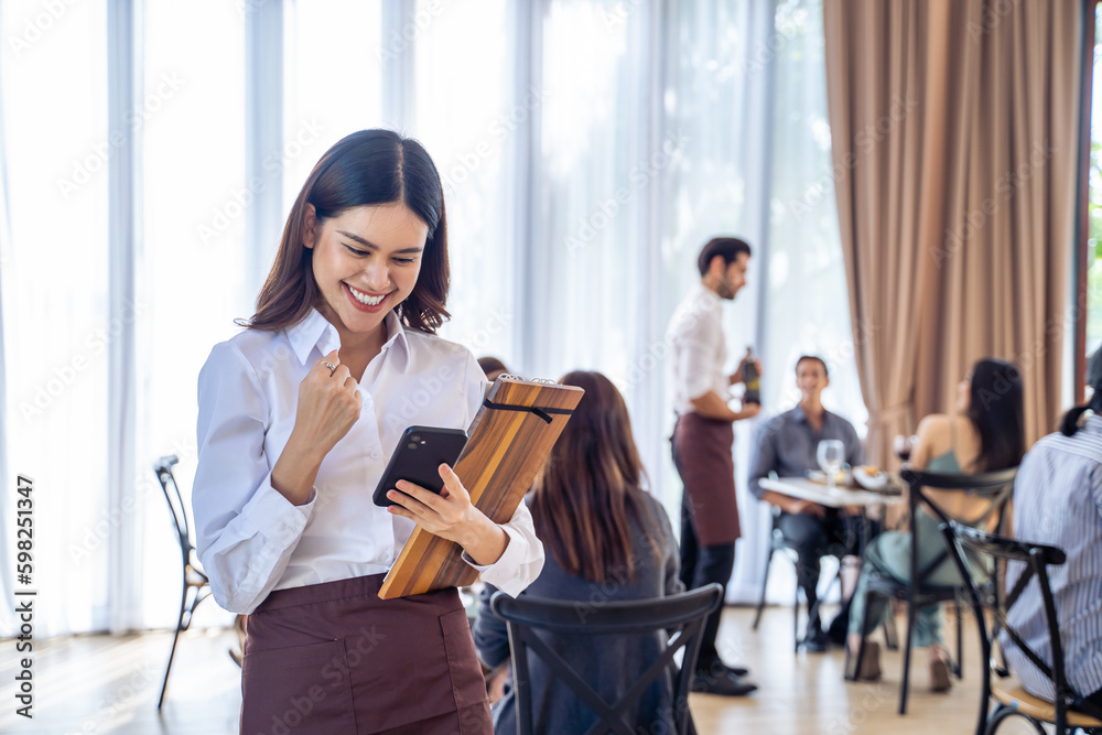 Asian beautiful waiter looking sale order on smartphone in restaurant. 