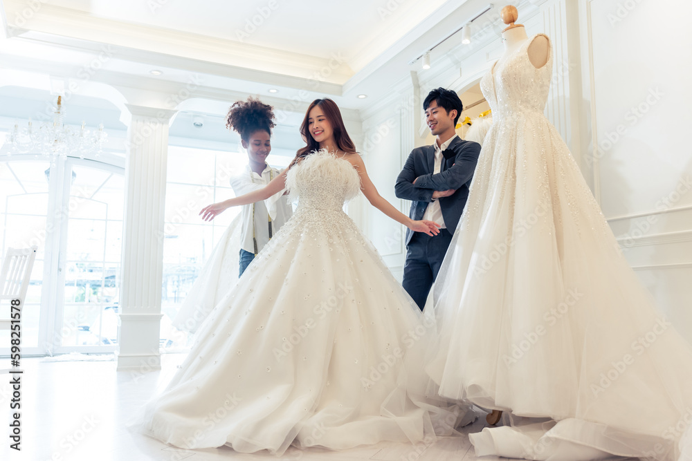 Asian beautiful bride trying on wedding gown with her fiance in studio. 