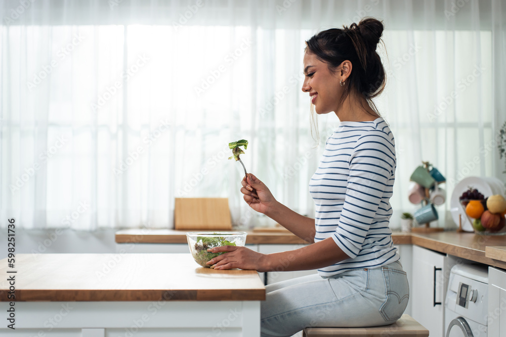 Caucasian young woman eating healthy green salad in kitchen at home. 