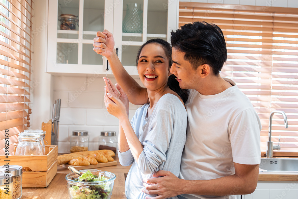 Asian romantic man making surprise girlfriend with necklace in kitchen. 