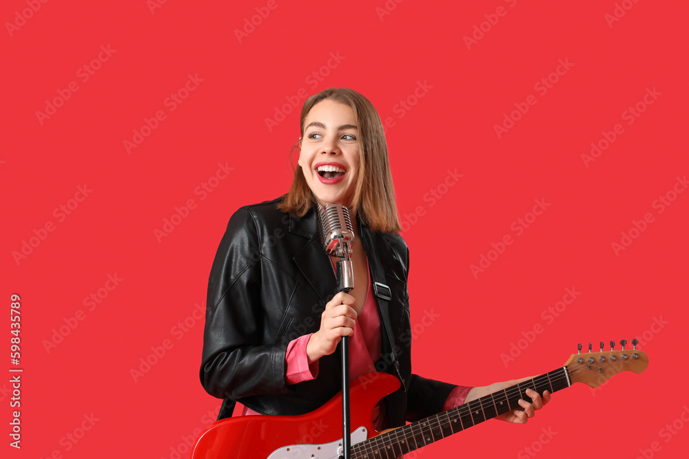 Young woman with guitar and microphone singing on red background