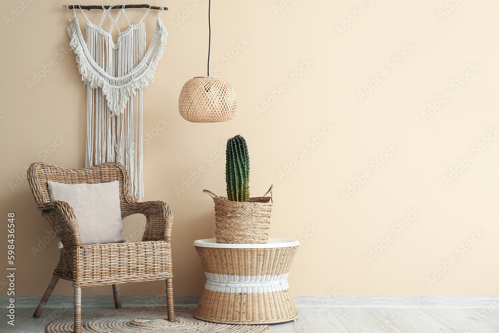 Cozy armchair, big cactus in pot on table and stylish macrame near beige wall