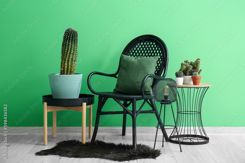 Stylish armchair, different cacti in pots and lamp near green wall