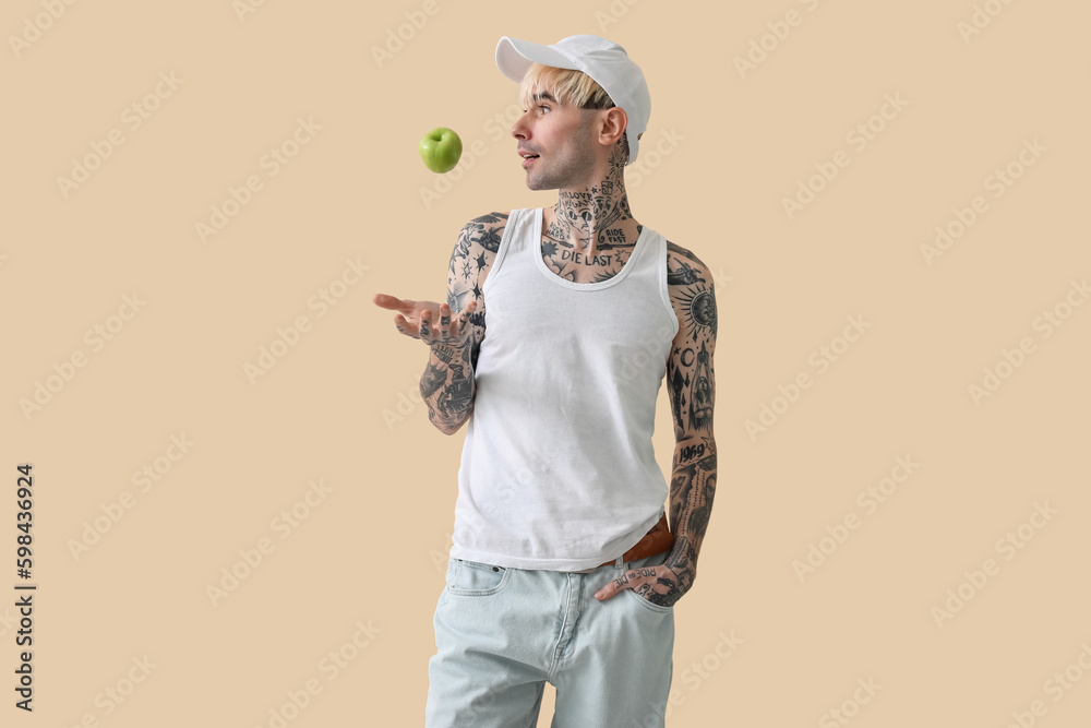 Tattooed young man with apple on beige background