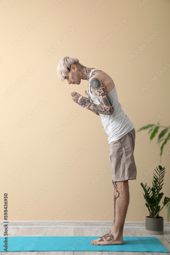 Tattooed young man doing yoga near beige wall