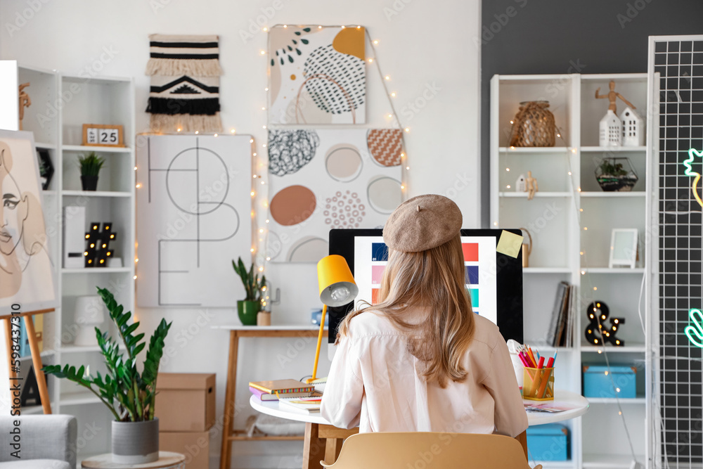 Female graphic designer working with computer at table in office, back view