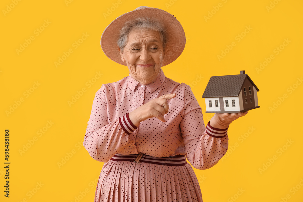 Senior woman with house model on yellow background