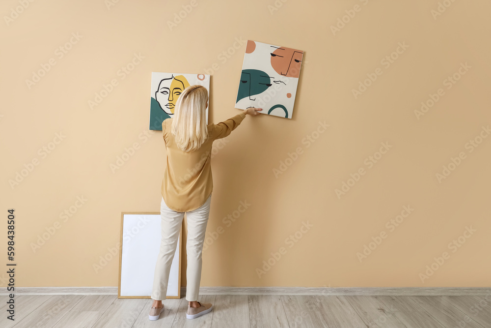 Mature woman hanging painting on beige wall, back view