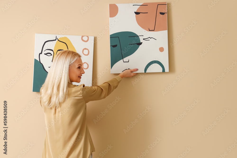 Mature woman hanging painting on beige wall