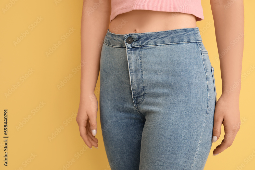 Young woman in stylish jeans on yellow background, closeup