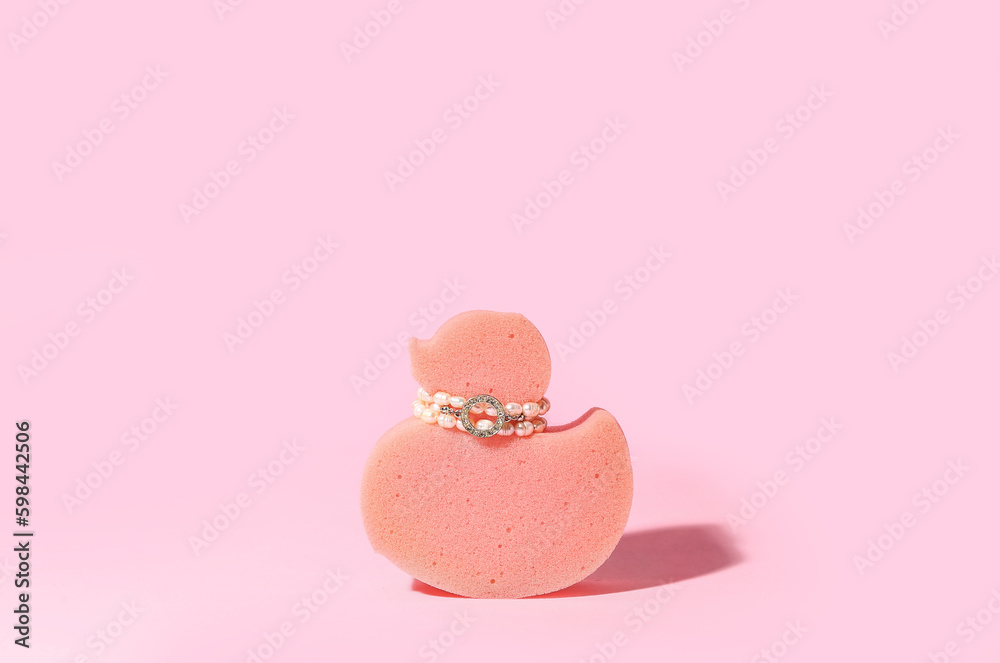 Sponge in shape of duck with jewelry on pink background