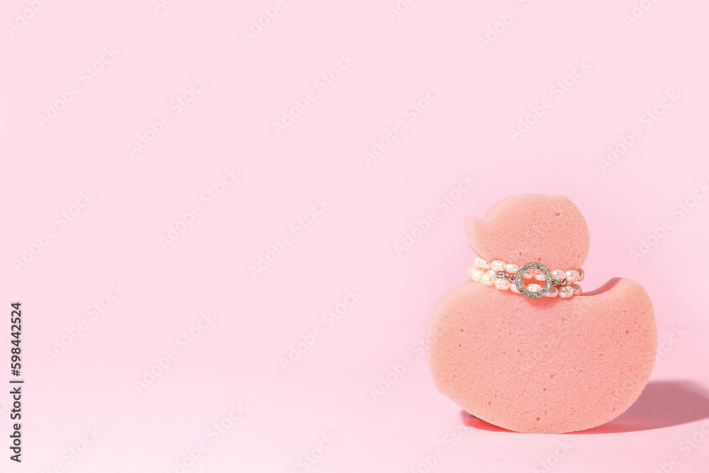 Sponge in shape of duck with jewelry on pink background