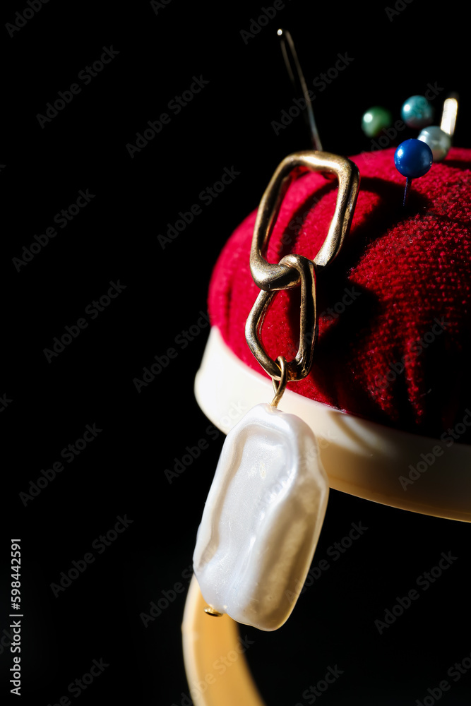 Pin cushion with earring on black background, closeup