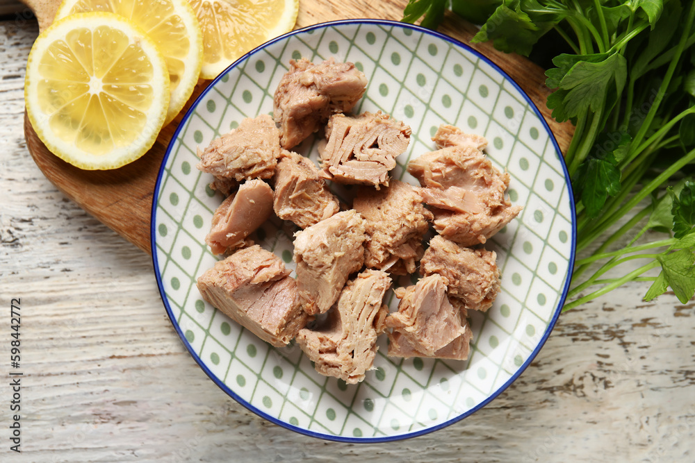 Plate with delicious canned tuna, lemons and parsley on white wooden table