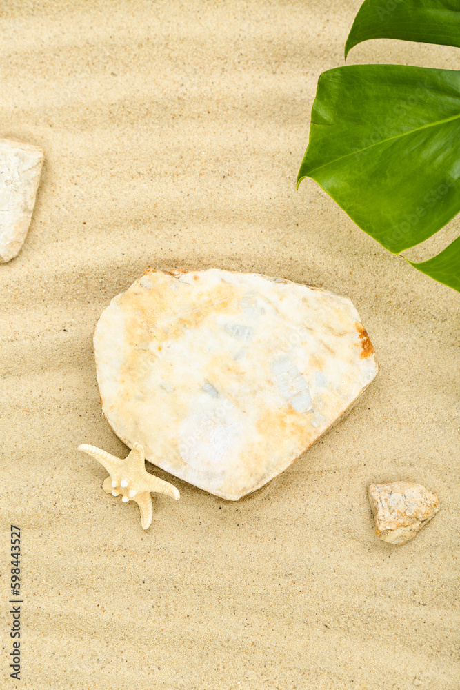 Decorative stone podium, starfish and tropical leaf in sand