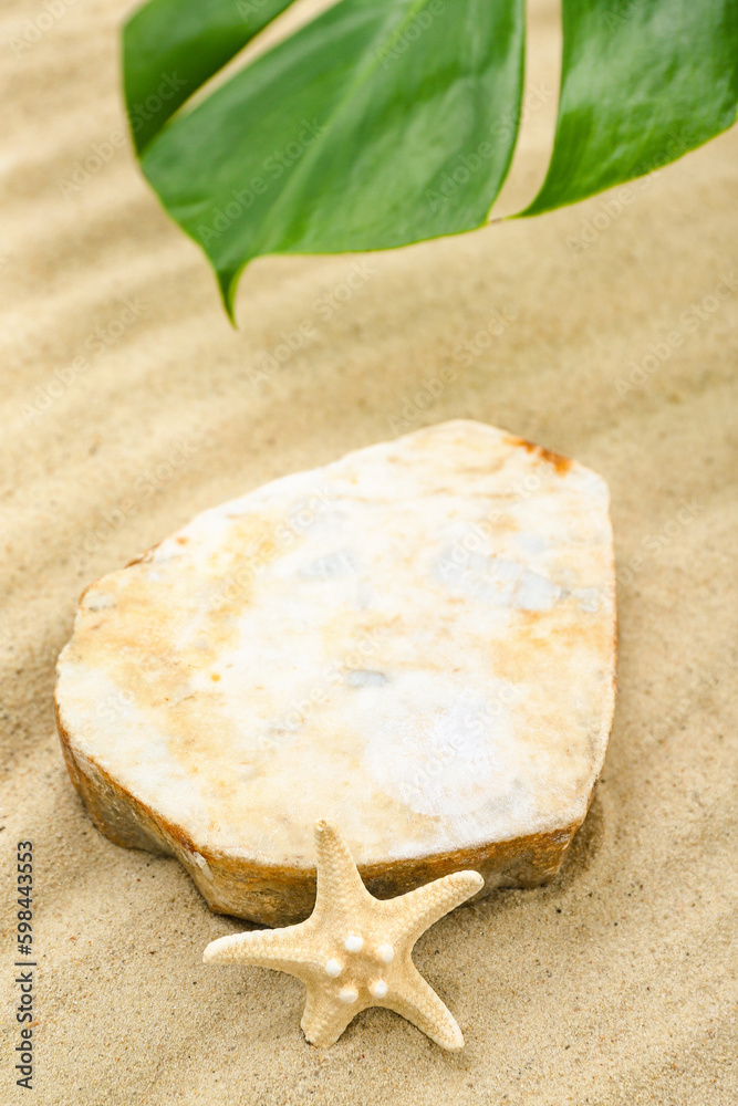 Decorative stone podium, starfish and tropical leaf in sand