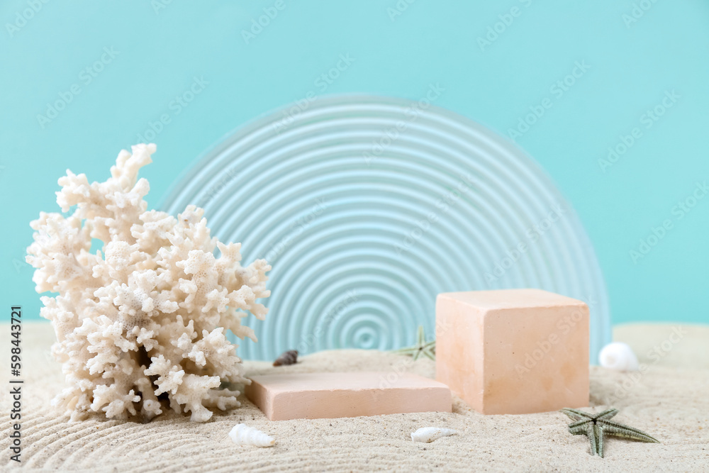 Decorative plaster podiums and coral in sand on turquoise background