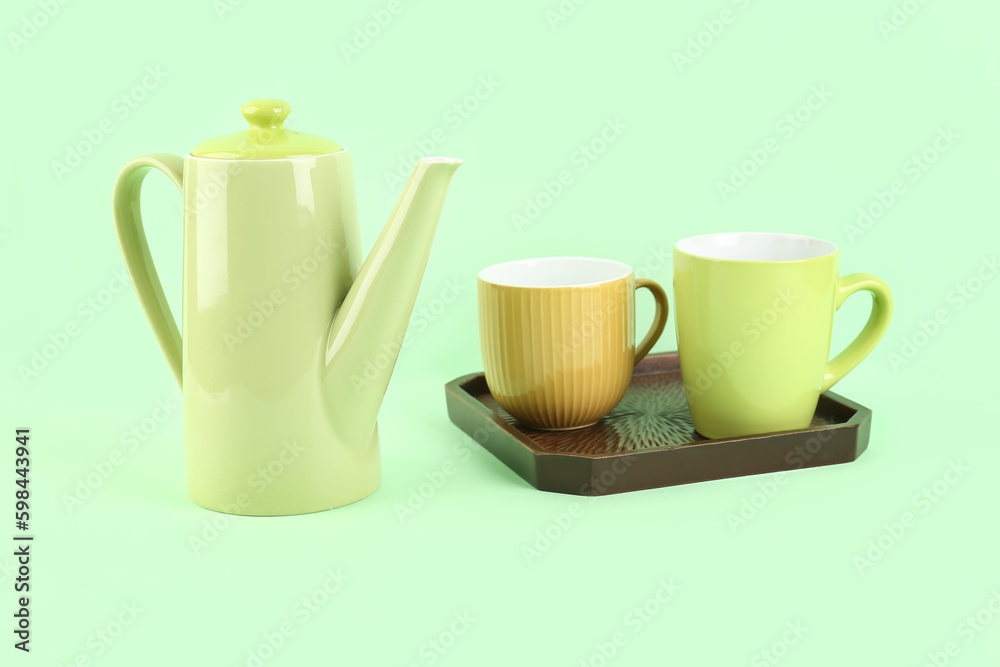 Teapot and tray with mugs on green background