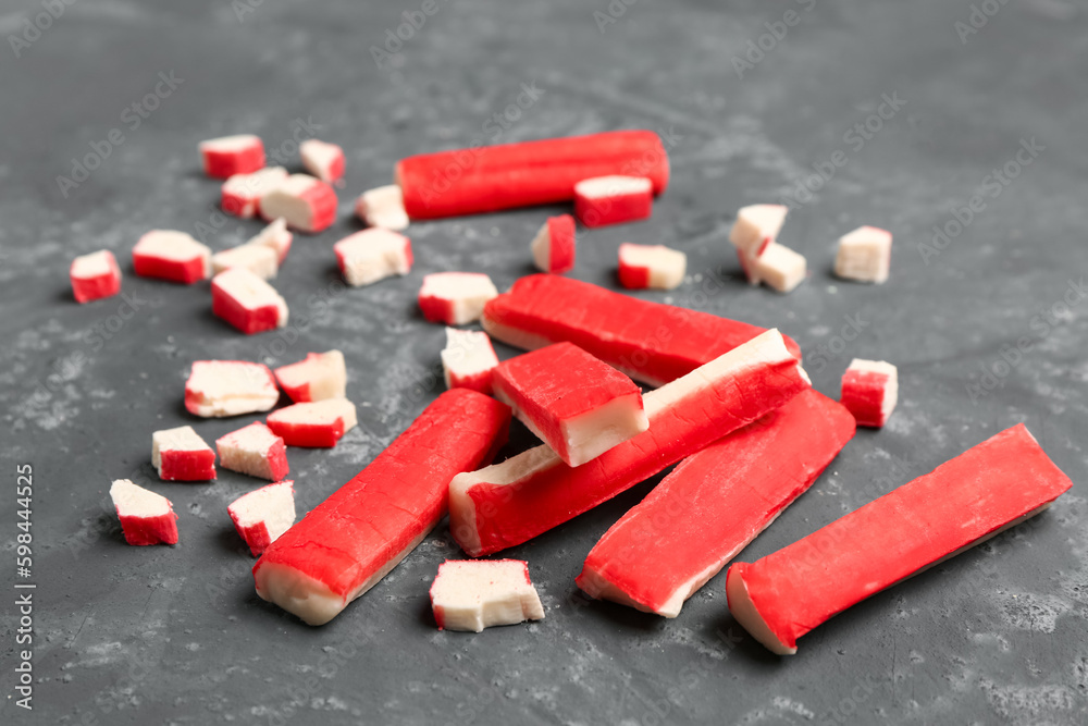 Tasty cut and whole crab sticks on green background