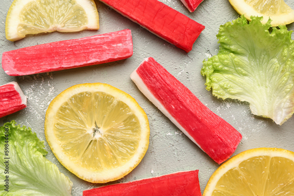 Tasty crab sticks, slices of lemon and lettuce on light background, closeup