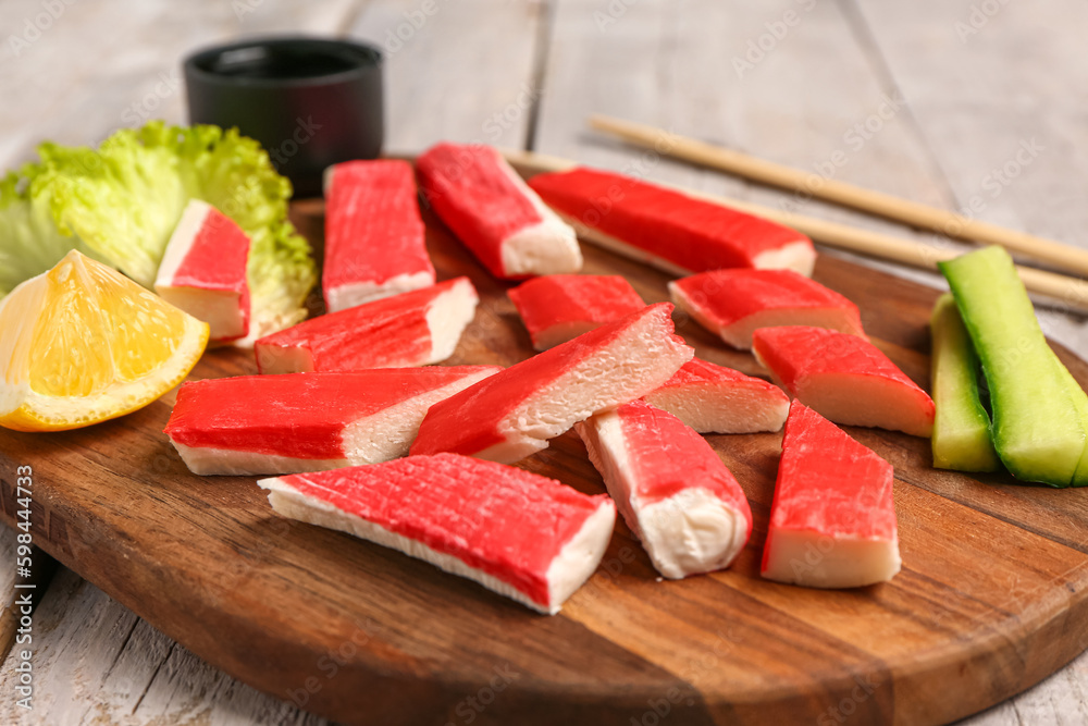 Board with tasty crab sticks on light wooden background