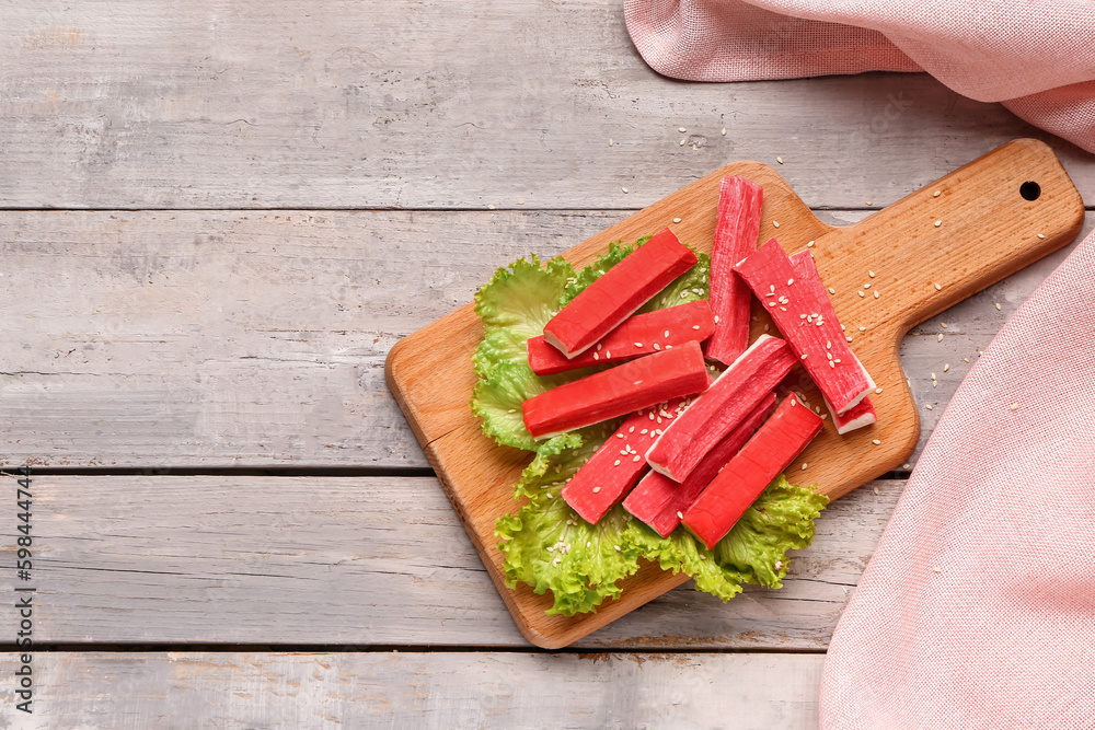 Board with tasty crab sticks on light wooden background